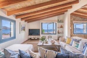 Un vaste espace de vie doté d’un haut plafond en bois, d’un ensemble de canapés, d’une table basse agrémentée d’objets décoratifs et d’un téléviseur.