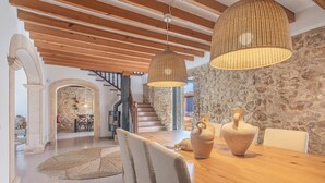 A dining area with a wooden table, chairs, and a stone wall. - Stone villa on the sea – Villa Can Cuarassa (Pollença)