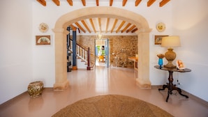 A hallway with a stone wall, wooden beams, a rug, a table with a lamp, and a vase. - Stone villa on the sea – Villa Can Cuarassa (Pollença)