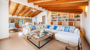 A spacious living room with a large sectional sofa, a coffee table, and a bookshelf. - Stone villa on the sea – Villa Can Cuarassa (Pollença)