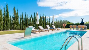 A swimming pool with lounge chairs and umbrellas, surrounded by trees and a barbecue area.