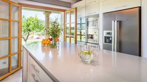 A modern kitchen with a large island, stainless steel appliances, and a view of greenery outside.