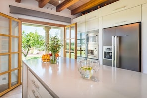 Une cuisine moderne dotée d’un grand îlot central, d’appareils électroménagers en acier inoxydable et offrant une vue sur la verdure environnante.