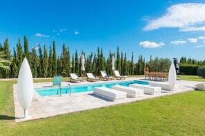 Une piscine avec des chaises longues, un petit espace aménagé et une pelouse.