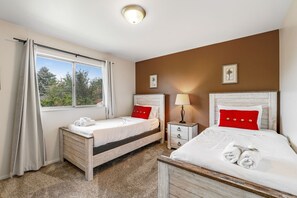 Una camera d'albergo con due letti, una finestra con tende, un comodino con una lampada e un piccolo comò di legno.