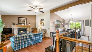 Un salon avec une cheminée, un téléviseur, un canapé et un coin repas comprenant des chaises et une table.