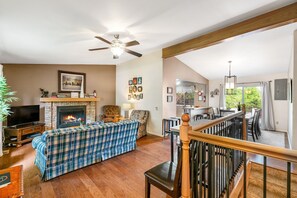 A living room with a fireplace, a television, a sofa, and a dining area with chairs and a table. - 4BD Cheyenne Mountain House with Hot Tub and Grill (Colorado Springs)