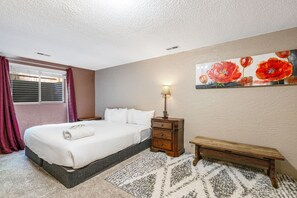 Un dormitorio con cama, mesita de noche, lámpara, banco y un cuadro en la pared.