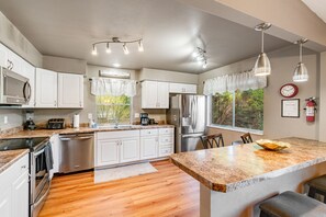 Una cocina moderna con armarios blancos, electrodomésticos de acero inoxidable, encimera de granito e iluminación colgante.