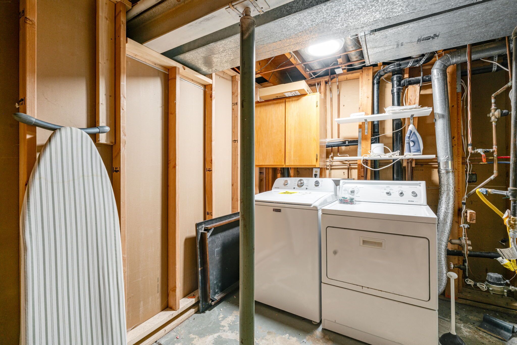 A laundry room with a washer and dryer, wooden cabinets, and visible plumbing.