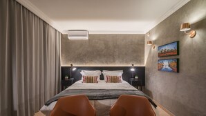 Quarto moderno com uma cama grande, duas mesas de cabeceira, ar condicionado fixado na parede e duas luminárias de parede.