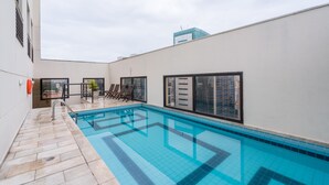 Uma piscina no terraço com água azul cristalina, rodeada por um muro branco e um deck revestido de azulejos.