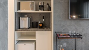 Quarto de hotel moderno com armário embutido, máquina de café, micro-ondas e televisão de ecrã plano fixada na parede.
