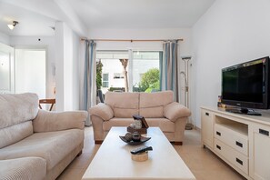 A living room with a sofa, a coffee table with decorative items, a television on a cabinet, and a view of the outdoors through a glass door.