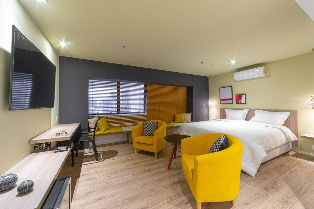 A modern hotel room with a bed, a desk, a chair, and a sofa.