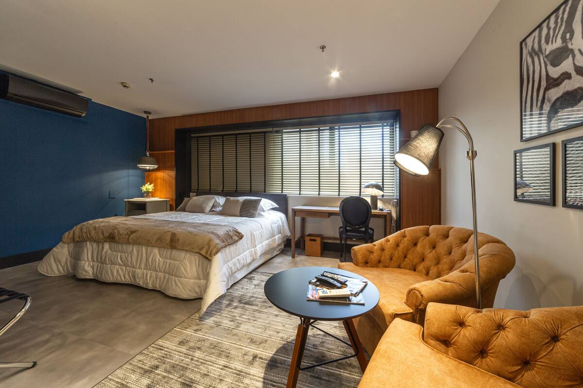 A modern hotel room with a large bed, a desk, a chair, and a small table.