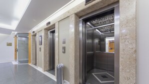 A modern elevator area with marble walls, a trash bin, and a digital display. - Cyclinn Faria Lima Itaim (São Paulo)