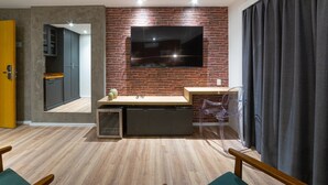 A modern living room with a brick wall, a flat-screen TV mounted above a wooden coffee table, and a clear plastic chair. - Cyclinn Faria Lima Itaim (São Paulo)