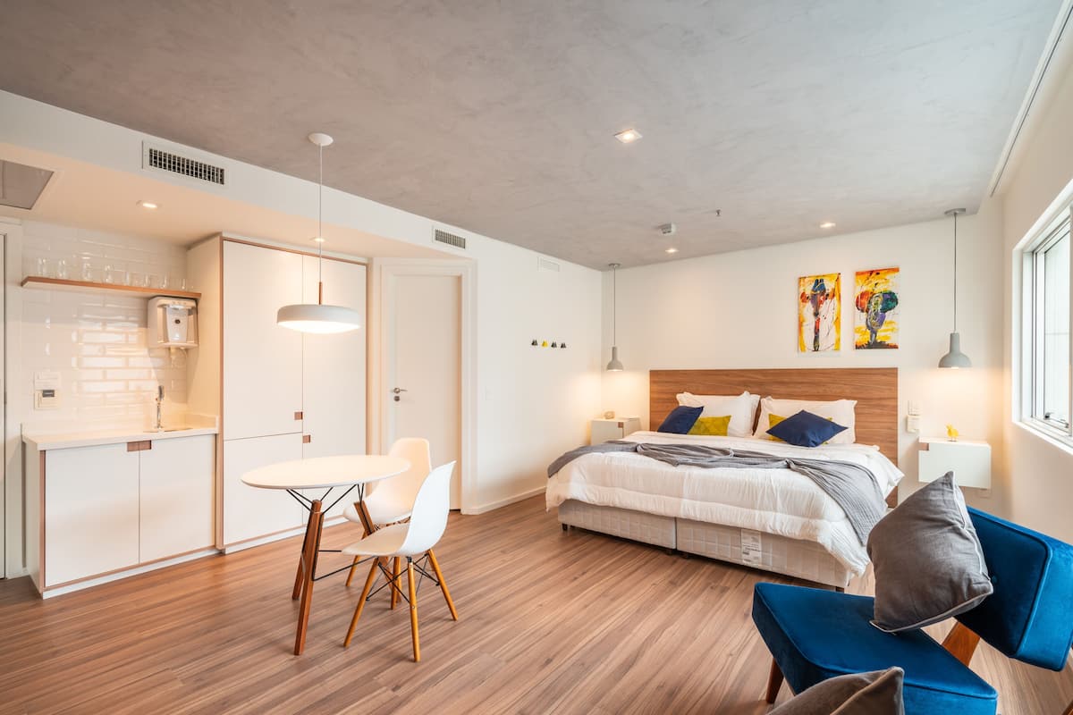 A modern hotel room with a bed, bedside tables, a desk, and a dining area.