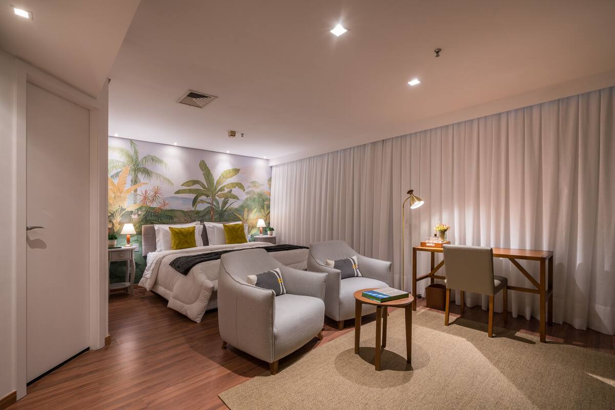 A hotel room with a bed, two armchairs, a desk, and a nightstand.