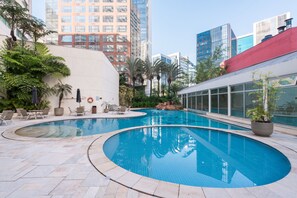 Un área de piscina con dos piscinas, sillones de descanso y un edificio con ventanas de vidrio al fondo.
