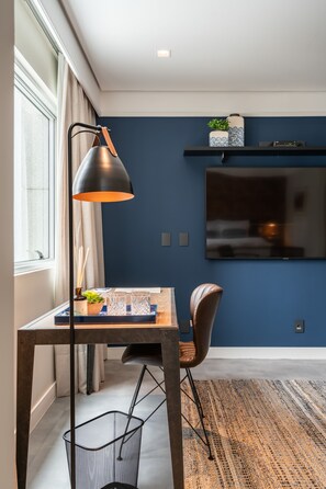 A modern room with a dark blue accent wall, a mounted TV, a wooden table with a chair, and a floor lamp.
