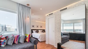 Moderni hotellihuone, jossa on suuri sänky, sohva ja parveke, jolta on näkymä kaupunkiin.