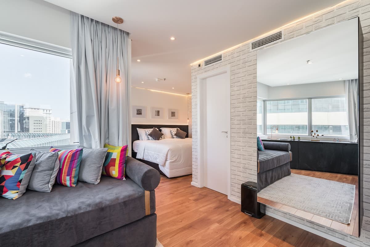 A modern hotel room with a large bed, a sofa, and a balcony with a view of the city.