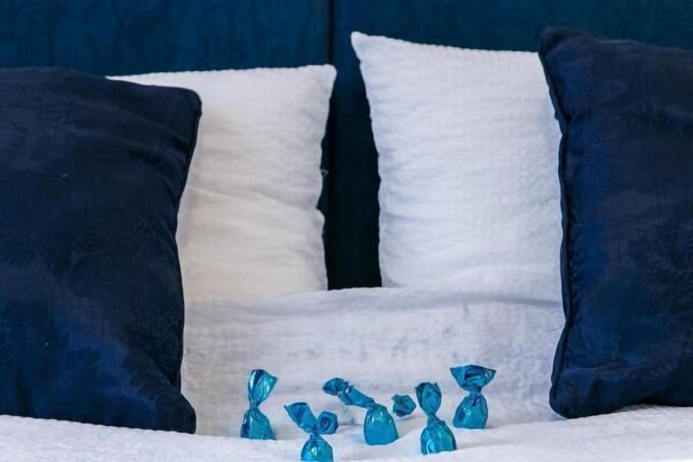 A bed with white and dark blue pillows, and several blue-wrapped items on the bed.