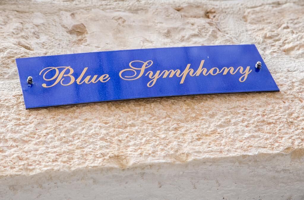 Een blauw bordje met de tekst 'Blue Symphony' vastgepind aan een oppervlak met structuur.