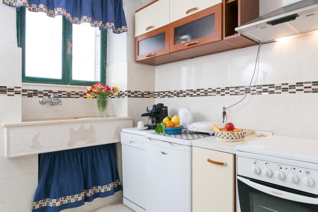 Una cucina compatta con lavastoviglie, fornello e finestra con tenda decorata.