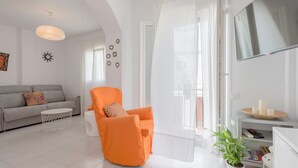 Un salon avec un canapé, un fauteuil orange, une plante en pot, un téléviseur et une bibliothèque.
