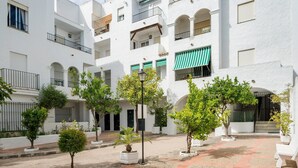 Une cour bordée de bâtiments blancs, dotée de balcons et agrémentée de plantes en pot.