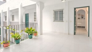 Un vaste couloir aux murs blancs, doté d’un sol carrelé et agrémenté de plantes en pot.