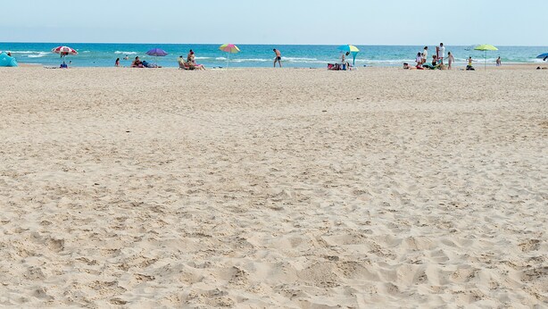 Une plage avec des gens, des parasols et l’océan.