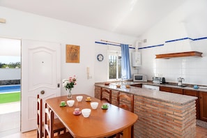 Une cuisine avec un îlot central en briques, des murs blancs et un coin repas comprenant des chaises et une table.