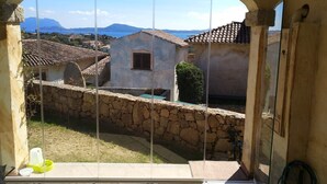 A room with a view through a glass door, stone walls, and a tiled roof. - Holiday Home 'Sardinia Sea View Pool & Spa' with Pool and Hot Tub (pittulongu)