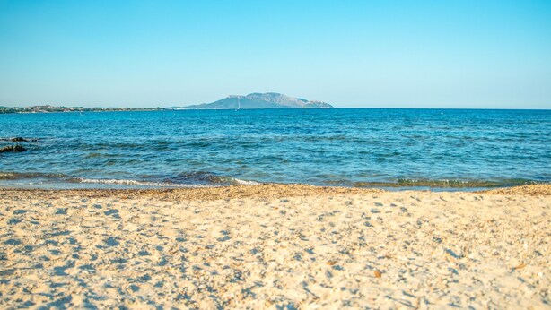 A beach with clear blue water, pebbly shore, and a distant mountain. - Holiday Home 'Sardinia Sea View Pool & Spa' with Pool and Hot Tub (pittulongu)