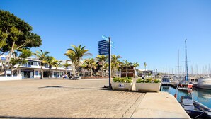Uma marina com barcos atracados, um calçadão pavimentado e um poste de sinalização com indicações.