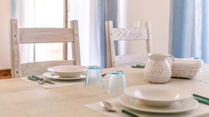 Taula de menjador preparada amb plats, gots i coberts, acompanyada de caires i una gerra decorativa.