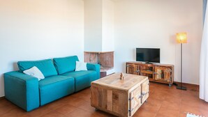 Un saló amb un sofà color turquesa, una taula baixa de fusta, una televisió i una làmpada de peu.