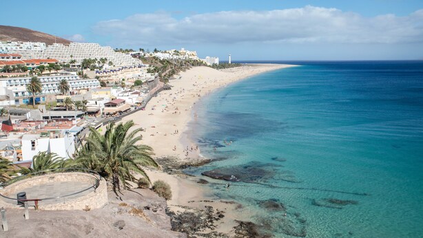 Un pueblo costero con playa, aguas azules cristalinas y edificios a lo largo de la costa.
