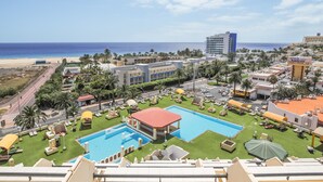 Un resort con una amplia piscina, varias zonas de descanso y vistas a la playa y al océano.