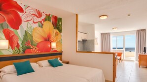 Habitación de hotel con cama, un gran mural floral, balcón con vistas y zona de comedor.