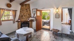 A cozy room with a stone fireplace, a wooden door leading outside, a small table with a white tablecloth, and a bench. - Fantastic Country Estate with Pool, Wi-Fi, Air Conditioning and Tennis Court (Pollensa)