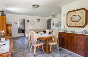 A dining area with a round table and wicker chairs, a wooden cabinet, and a kitchen in the background.