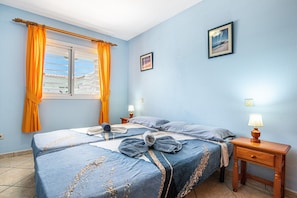 Un dormitorio con dos camas, una ventana con cortinas, una mesita de noche con lámpara y un cuadro colgado en la pared.