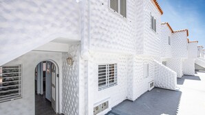 A white building with a tiled roof, a door, and a window. - Lovely Apartment Close to the Beach with Terrace, Garden & Wi-Fi (Costa Calmar, Fuerteventura)
