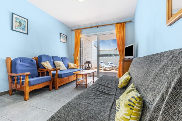 Ein Wohnzimmer mit einer Couch, Sesseln, einem Tisch und einem Fernseher.