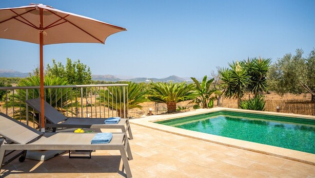 Ein Poolbereich mit Liegestühlen und Sonnenschirm, mit freiem Blick auf den Pool und umgebender Bepflanzung.